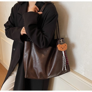 Detail of a large brown tote bag with a plush bear charm and woven lanyards on shoulder