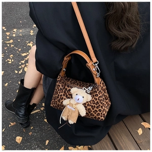 Detail of leopard print dumpling bag with a cute plush bear pendant on a wooden bench