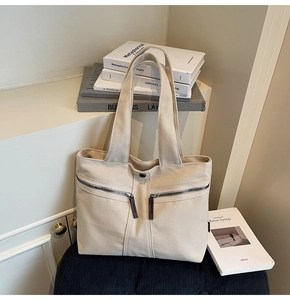 Detail of canvas tote bag showing dual front zipper pockets with leather pull tabs