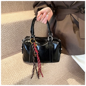 Détail d'un sac Boston noir en cuir huilé avec breloque tressée et boucles en métal