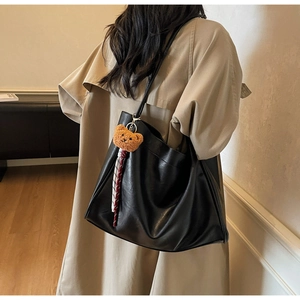 Detail of black faux leather tote bag featuring a cute brown teddy bear plush pendant