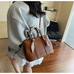 Macro view of dark brown pebbled leather bucket bag with printed silk scarf on handle