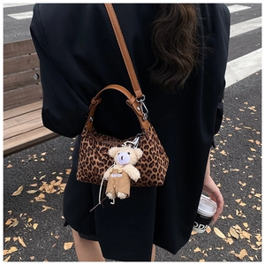Close-up of leopard print dumpling bag featuring leather handles and cute plush bear charm
