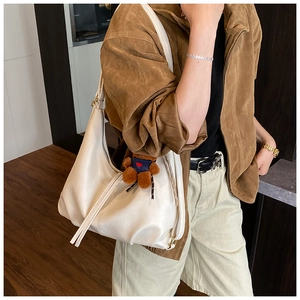 Close-up of cream faux leather shoulder bag featuring side drape and brown plush bear charm