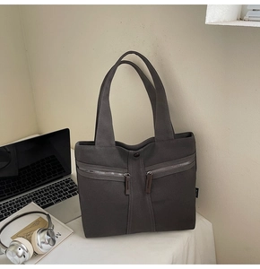 Detail of grey canvas tote bag featuring double parallel zipper pockets and side tag