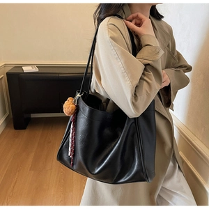 Detail of black faux leather tote bag showing fine texture and plush tassel accessory