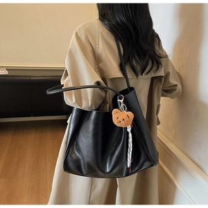 Detail of black soft leather tote bag with brown plush bear charm and plaid ribbon accent