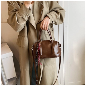 Brown glossy leather crossbody bag with woven tassel detail on a khaki trench coat background
