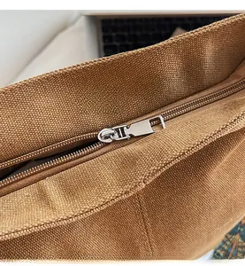Detailed close-up of smooth silver metal zipper on premium brown canvas tote bag texture
