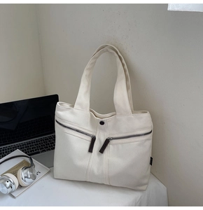 Off-white canvas tote bag with side zip pockets shown with a laptop and books