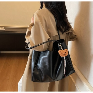 Detail of a large black faux leather tote bag with a plush bear charm on a model