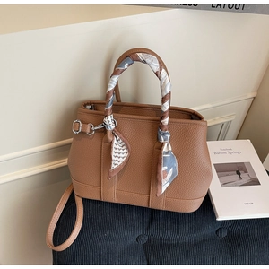 Detailed view of a brown pebbled leather handbag with a decorative silk scarf on handle