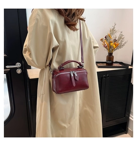 Borsa a secchiello bordeaux indossata con trench beige per un look a tracolla
