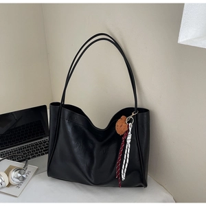 Detail of a black leather tote bag with a brown bear charm and braided rope accessory