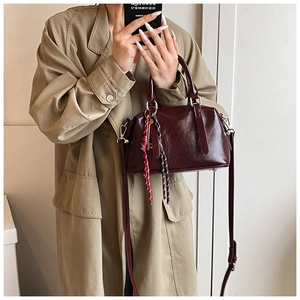 Sac Boston en cuir huilé bordeaux porté sur un trench-coat pour un look élégant