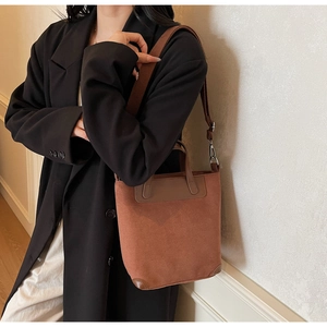 Detail of brown suede tote bag featuring a leather handle and a wide woven shoulder strap