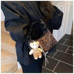 Close-up of leopard print handbag with a plush bear charm and black leather handle