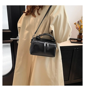 Dettaglio borsa a tracolla nera con zip argentate abbinata a un trench beige