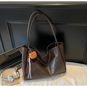 Detail of dark brown leather tote bag showing large capacity and soft texture with charms