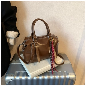 Vue détaillée d'un sac Boston marron foncé avec charme gland posé sur une valise