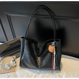 Detail shot of black leather tote bag with bear pendant on white fabric background