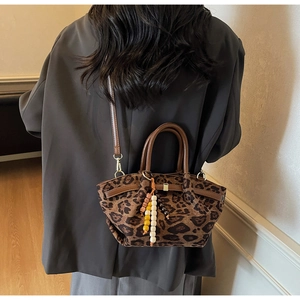 Detail of leopard print tote bag featuring a beaded tassel charm and leather shoulder strap
