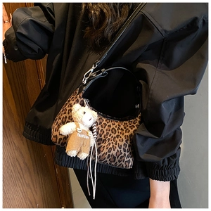 Close-up of leopard print dumpling bag with a cute plush bear charm and black strap