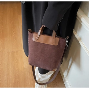 Close-up of a dark brown suede tote bag with leather trim and wide fabric shoulder strap