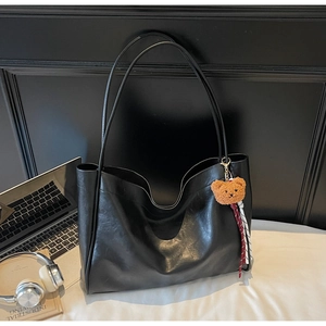 Close-up of black leather tote bag with brown bear charm in office workplace setting