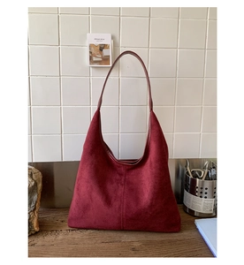 Detail of burgundy suede tote bag on a wooden table with elegant minimalist design