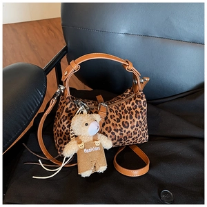 Detail of leopard print handbag with brown leather handles and cute teddy bear pendant