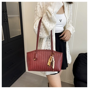 Detail of burgundy woven tote bag featuring an ethnic beaded charm and texture