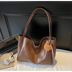 Macro detail of brown leather tote bag featuring a cute bear charm and woven tassel accent