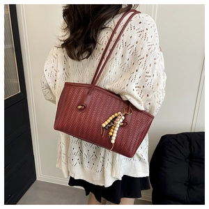Burgundy woven tote bag detail showing the leather texture and beaded tassel charm on a model