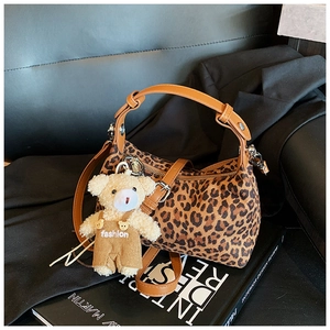Detail of leopard print handbag with leather handles and cute plush bear charm accessory