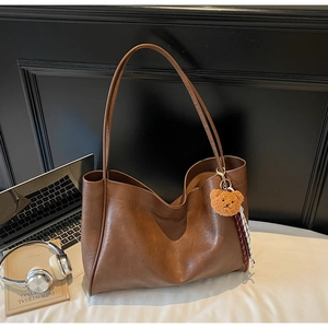 Detail of a large brown faux leather tote bag with a plush bear charm and striped ribbon