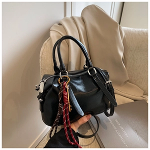Détail du sac Boston noir brillant avec cordon tressé bicolore et breloque clé dorée