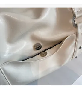 Close-up of glossy off-white leather bag featuring a polished silver magnetic metal clasp