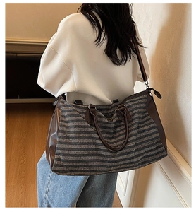 Gray striped gym bag with brown leather trim shown on shoulder by a model outdoors