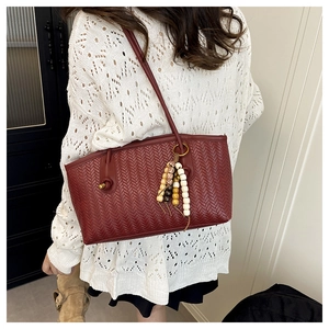 Detail of burgundy woven texture tote bag with ethnic beaded charm accessory