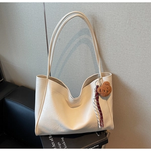 Detail view of cream white leather tote bag featuring brown plush bear and woven tassels