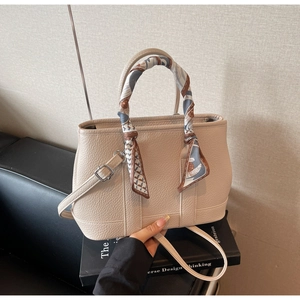 Close-up of cream pebble leather handbag with decorative silk scarf and silver hardware