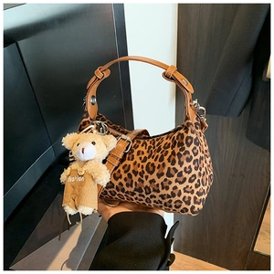 Detail of leopard print handbag with brown leather handle and cute plush bear charm