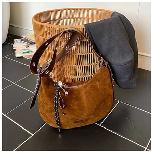 Détail du sac hobo en daim marron avec bandoulière à œillets et breloque tissée