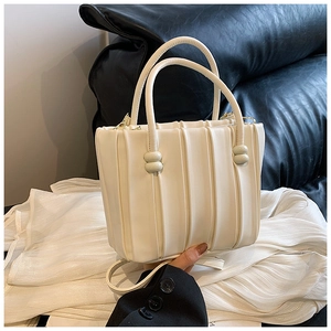 Detail of cream pleated bucket bag showing bead accents and vertical texture finish