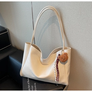 Detail of off-white leather tote bag with brown plush bear charm and woven rope accent