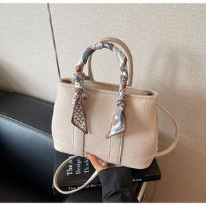 Close-up of beige lychee grain leather tote bag with silk scarf wrapped around handle