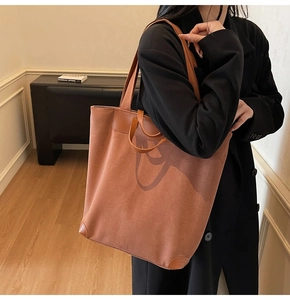 Detail of a large brown faux suede tote bag featuring reinforced handles and a long shoulder strap