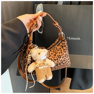 Detail of leopard print hobo bag featuring brown leather strap and plush bear charm