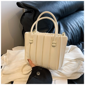 Detail view of cream-colored bucket bag with vertical pleated texture and round handles